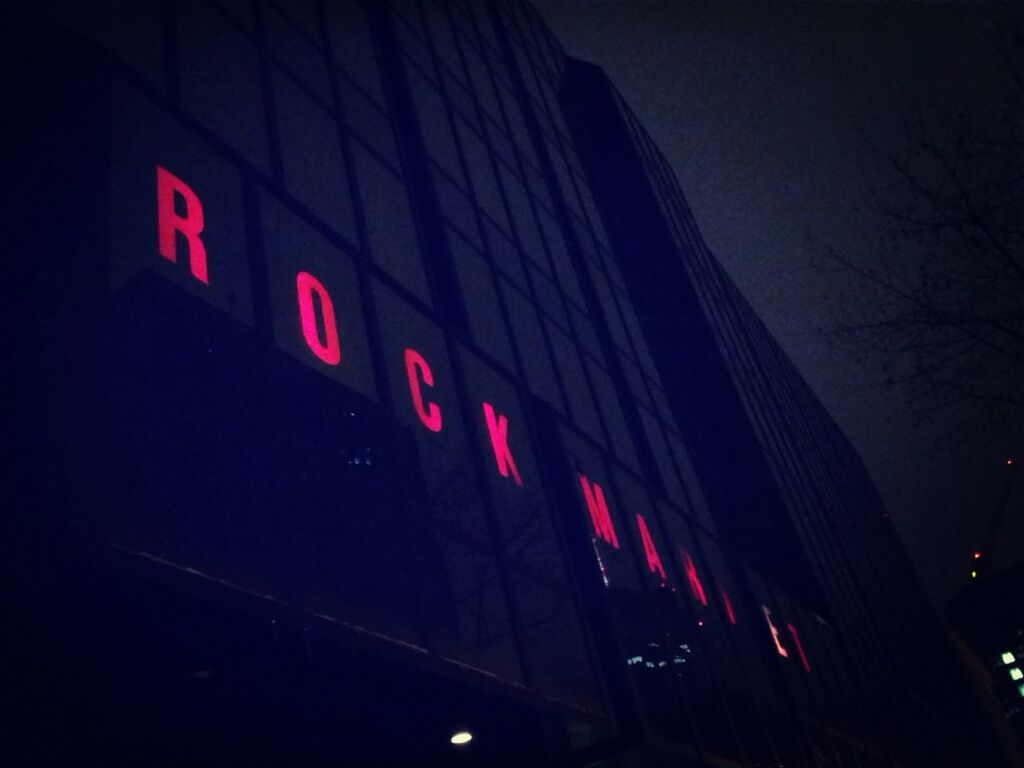 illuminated, night, architecture, low angle view, building exterior, built structure, text, western script, city, lighting equipment, sky, communication, red, street light, outdoors, dark, street, building, guidance, clear sky