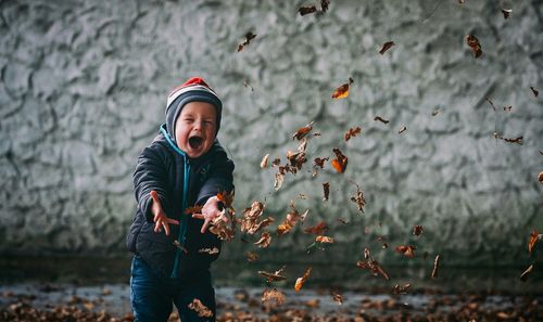 Preschool boy in warm clothing throwing autumn leaves in mid-air