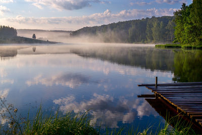 Scenic lake against sky wide angle shot with wooden pier and sky reflection in still water surface