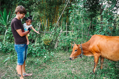 Woman carrying daughter while standing with cow at farm