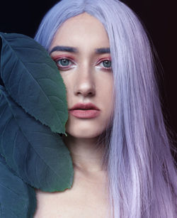 Close-up portrait of young woman with dyed hair against black background