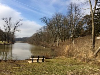 Bench by lake against sky