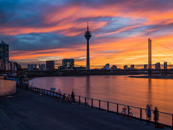 Bridge over river by buildings against sky during sunset