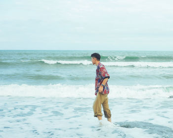 Rear view of woman standing at beach against sky