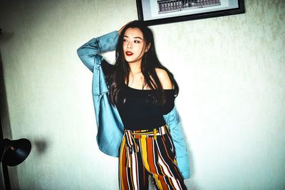 Young woman with long hair looking away while standing against wall