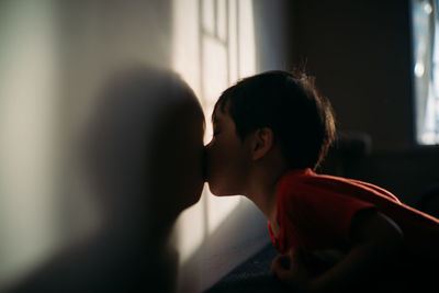 Side view of boy kissing on wall at home