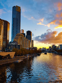 City by river against sky during sunset