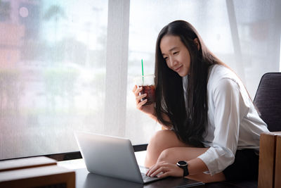 Young woman using phone while sitting on table