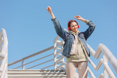 Low angle view of woman with arms raised standing against sky