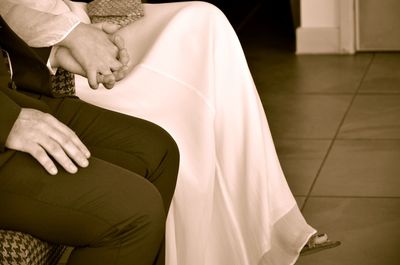 Cropped image of couple holding hands while sitting on bed at home