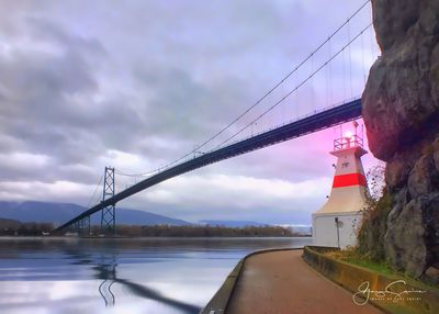 Electricity pylon by bridge against sky