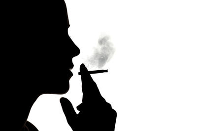 Close-up of silhouette man smoking cigarette against white background