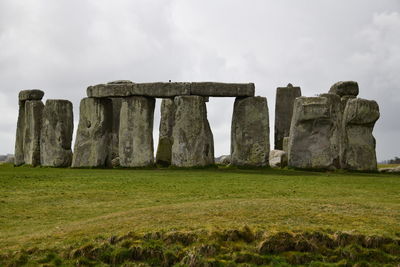 Stone structure on grassy field against cloudy sky