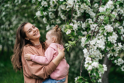 Young mother with her daughter in her arms in a blooming apple orchard