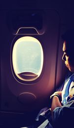 Young man looking through window while traveling in airplane