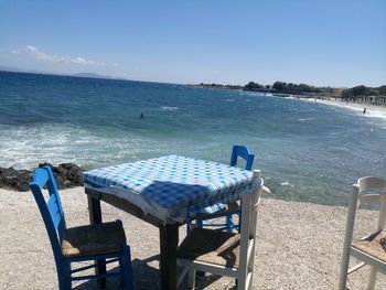 Chairs and table on beach against clear blue sky