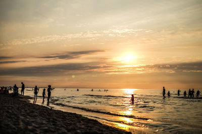 Silhouette people on beach against sky during sunset