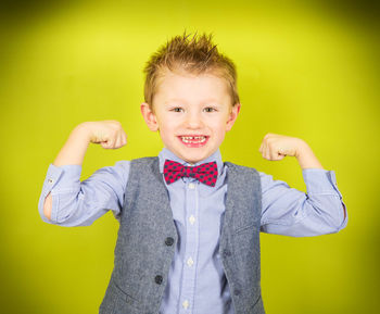 Portrait of smiling boy flexing muscles against yellow background