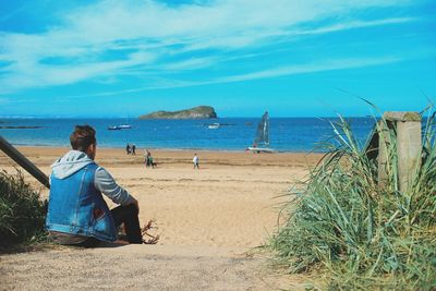 Rear view of man sitting at beach against sky