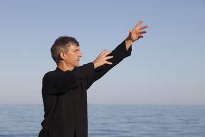 Mature man exercising at beach against clear sky