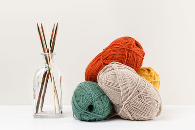 Bamboo knitting needles in glass jar and red, green, yellow and beige clews of yarn. selective focus