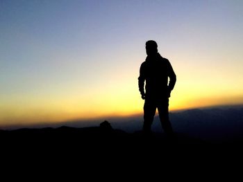 Silhouette man standing on landscape against clear sky during sunset