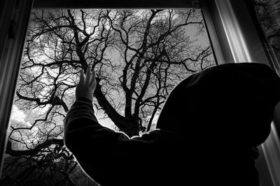 Child in hooded jacket waving towards bare tree from window