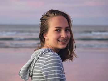 Portrait of smiling young woman at beach against sky