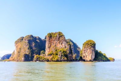 Rock formation in sea against clear blue sky