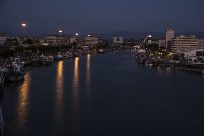 Illuminated buildings by river against sky at night