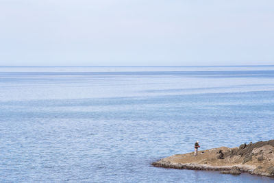 Mid distance view of man standing on rock formation in sea