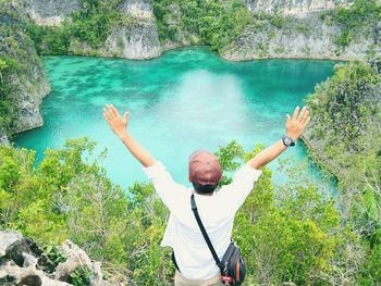 High angle view of man with arms raised standing against lake in forest