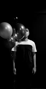 Midsection of man holding balloons against black background