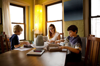 Mother sitting with sons doing homework at table