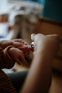 Cropped woman cutting son fingernail at home