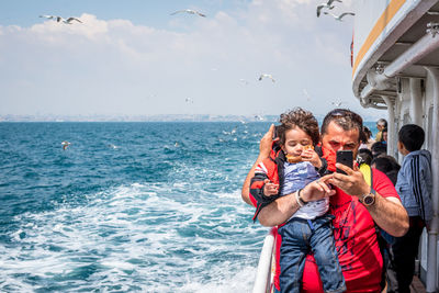 Full length of father and son in sea against sky