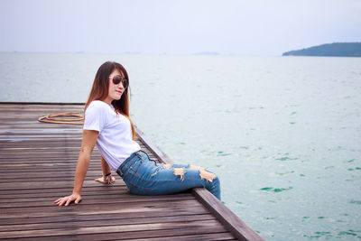 Young woman sitting on shore against sea