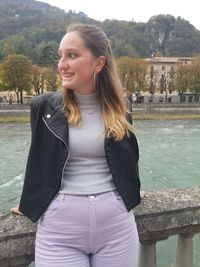 Young woman smiling while standing against trees at shore