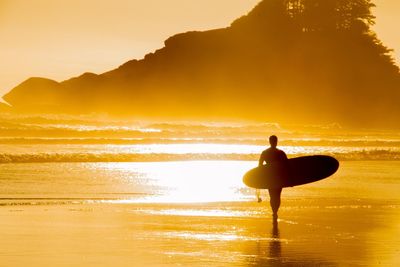 Silhouette woman standing on beach against sky during sunset