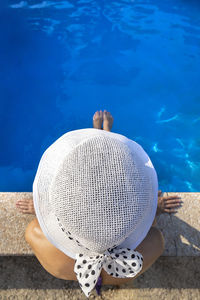 Top view of a woman with a white hat seated on the edge of a swimming pool.
