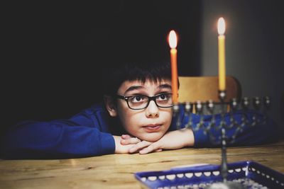 Boy wearing eyeglasses while looking at lit candles at home
