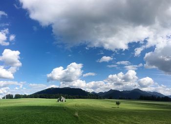 Scenic view of vast green field and house against cloudy sky