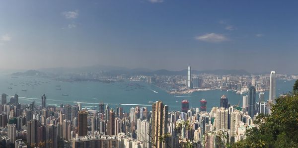 High angle view of cityscape by sea against blue sky