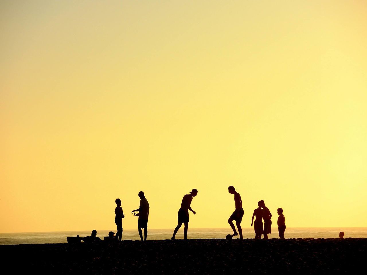 SILHOUETTE PEOPLE PLAYING SOCCER ON BEACH AGAINST CLEAR SKY