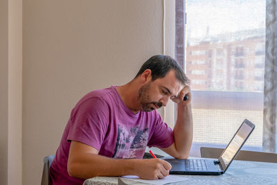 Young man using phone while sitting on table at home