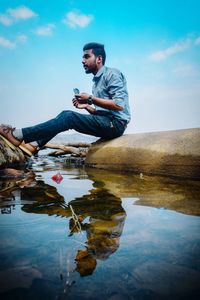 Man sitting on rock at stream against sky