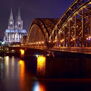 Illuminated cologne cathedral and hohenzollern bridge over rhine river at night