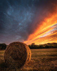 Hay bales on field against sky during sunset