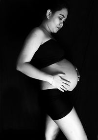 Side view of pregnant woman standing against black background