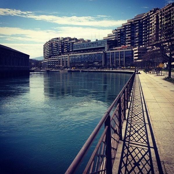 architecture, built structure, building exterior, water, city, sky, river, bridge - man made structure, connection, canal, railing, transportation, building, waterfront, city life, bridge, reflection, outdoors, cloud - sky, diminishing perspective